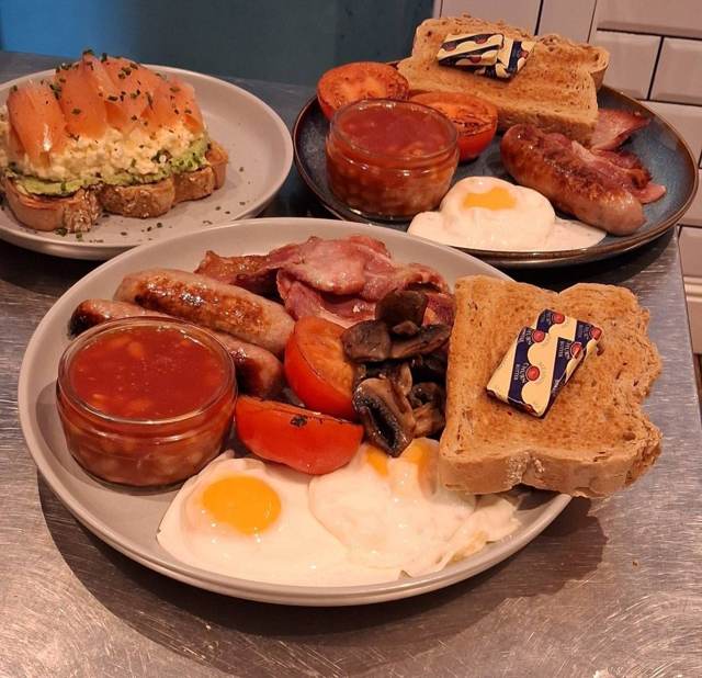 A full English breakfast with a plate of smoked salmon and avocado on toast behind