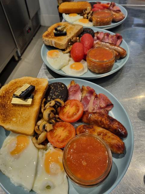 Three full English breakfast plates lined up on the pass